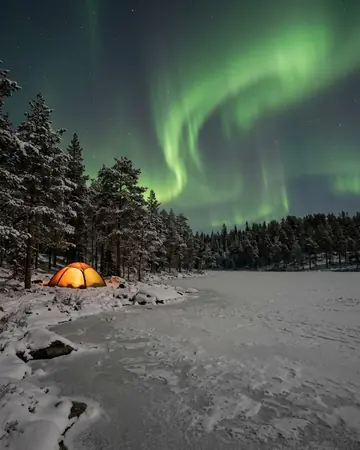 Green aurora over a frozen lake with snowy pines, a single tent glowing warm at the shore, no people. Photographed without a preset.
