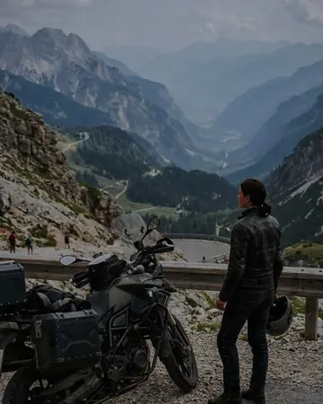 A fictional motorcyclist in a leather jacket stopped at a mountain pass overlook, bike in the foreground, hazy valley. With the Chrome Film preset applied.