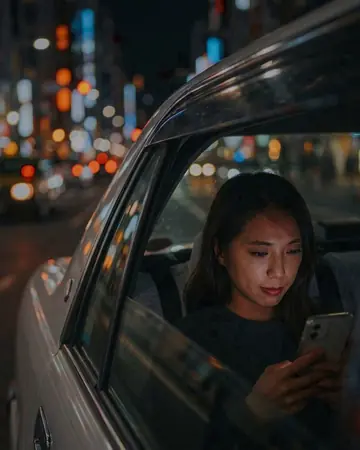 View through a taxi window at night, city lights bokeh, fictional passenger's face lit by the phone. With the Cinema Grade preset applied.