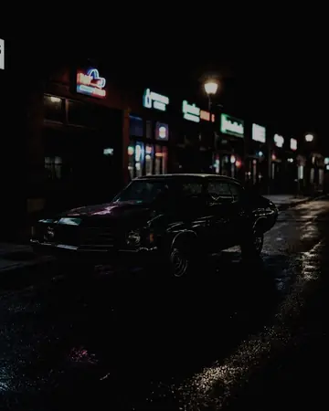 A 1970s classic car parked on a night street lit by neon shop signs, wet asphalt reflections, no people. With the Japan Film preset applied.
