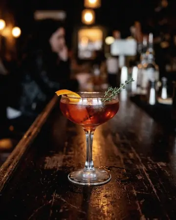 A garnished cocktail on a dark bar top with soft amber backlight. With the Japan Film preset applied.