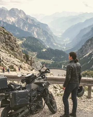 A fictional motorcyclist in a leather jacket stopped at a mountain pass overlook, bike in the foreground, hazy valley. With the Japan Film preset applied.
