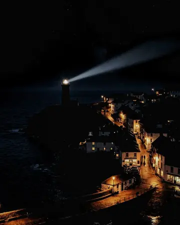 A lighthouse beam sweeping a starry sky, night, lit only by street and shop lights. With the Japan Film preset applied.