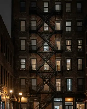 A fire escape zigzagging up a brick facade, night, lit only by street and shop lights. Photographed without a preset.