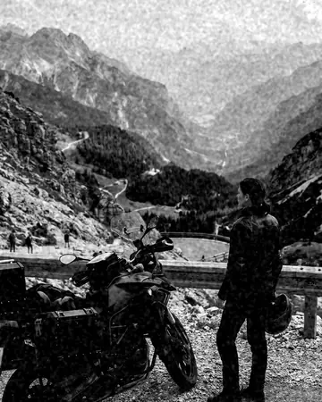 A fictional motorcyclist in a leather jacket stopped at a mountain pass overlook, bike in the foreground, hazy valley. With the Mono Film preset applied.