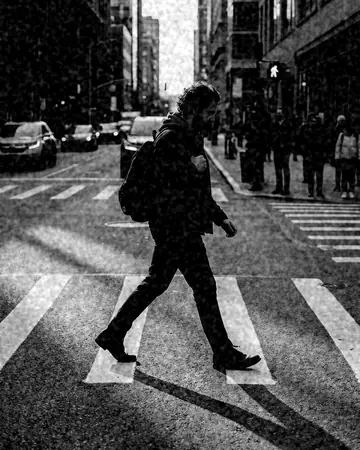 A fictional man walking a city crosswalk with long afternoon shadows. With the Mono Film preset applied.