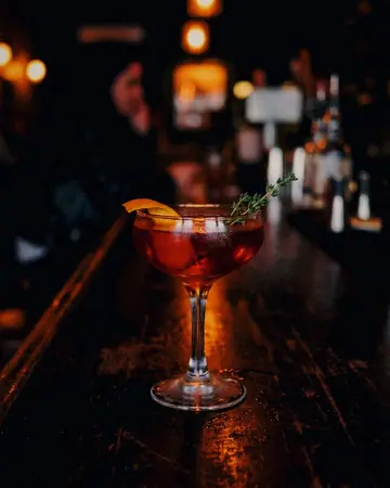 A garnished cocktail on a dark bar top with soft amber backlight. With the Night Halation preset applied.