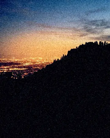 City light pollution glowing behind a dark hill, blue hour just after sunset, cool ambient light. With the Night Halation preset applied.