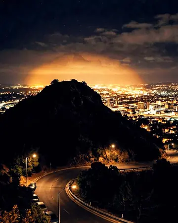 City light pollution glowing behind a dark hill, night, lit only by street and shop lights. With the Night Halation preset applied.