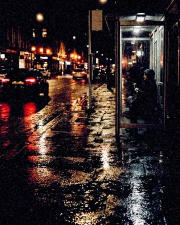 A bus stop on a wet pavement, reflections in the puddles, night, lit only by street and shop lights. With the Night Halation preset applied.
