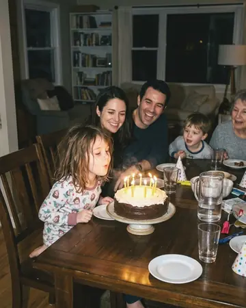 A fictional child blowing out birthday candles, direct flash at night, family around the table. With the Pastel Film preset applied.
