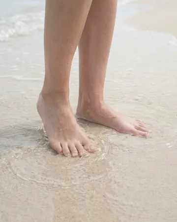 Bare feet in shallow clear water on pale sand, daylight. Photographed without a preset.