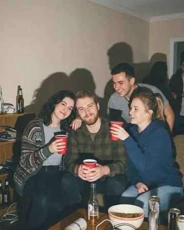 A fictional group of friends at a house party at night, shot with direct on-camera flash, hard shadows on the wall, red cups. With the Warm Negative preset applied.