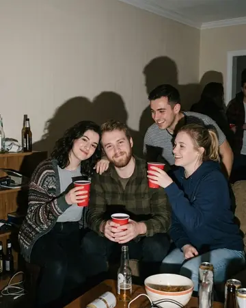 A fictional group of friends at a house party at night, shot with direct on-camera flash, hard shadows on the wall, red cups. Photographed without a preset.