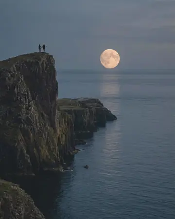 A full moon rising over sea cliffs at dusk, calm sea, a fictional couple as tiny silhouettes on the edge. With the Warm Negative preset applied.